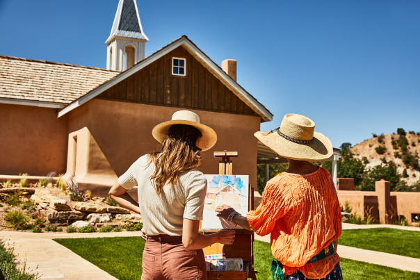 Two women paint a watercolor of Archbishop Lamy's Chapel.