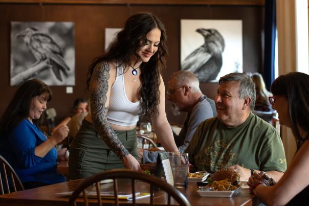 A waitress places a plate of food on a restaurant table in front of a smiling customer.