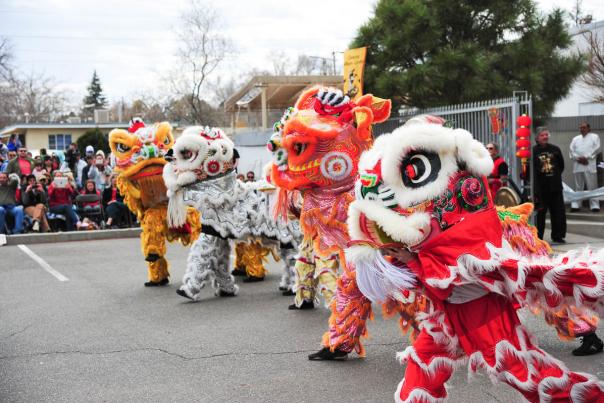 Four vibrant lion dancers in colorful costumes perform energetically on a street, captivating a crowd of spectators, celebrating a festive occasion.
