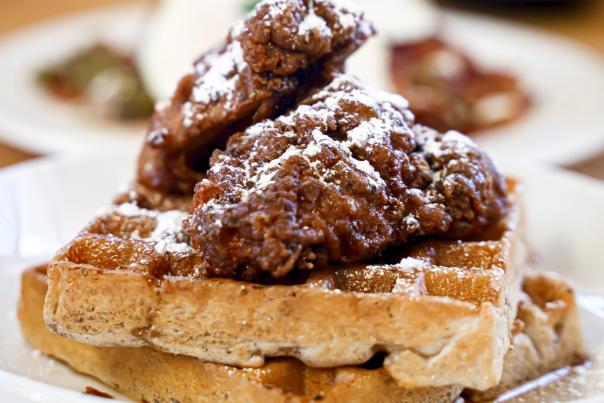 A plate with a waffle topped with crispy fried chicken and powdered sugar.