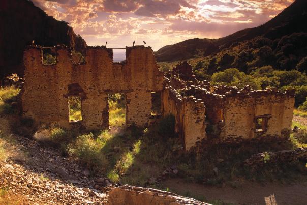 The sunlit Van Patten Ruins in a green valley, silhouetted against a dramatic sunset sky.