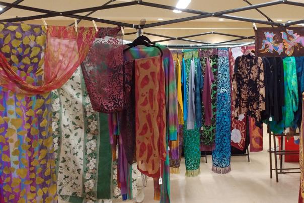 A clothing rack is full of colorful shirts, scarves, and fabrics.