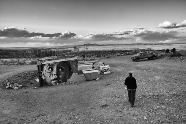 A black and white photo of a man walking away in a desert landscape.