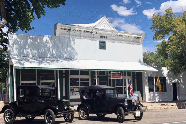 Two vintage cars parked in front of a historic 1896 building with museum signs.