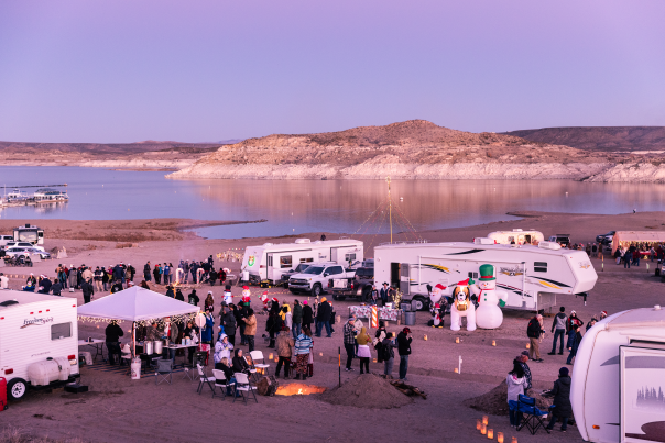 People gather and celebrate near RVs decorated for the holidays with Elephant Butte Lake in the background.
