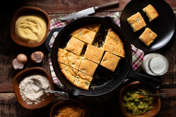 Gluten-Free Green Chile Cornbread in a cast iron skillet surrounded by raw ingredients.