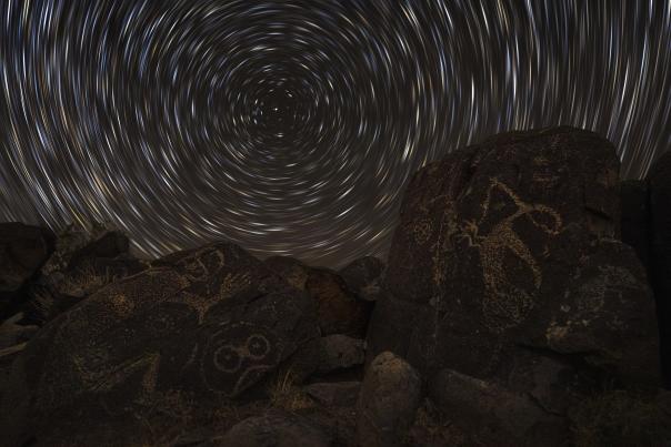Petroglyphs on dark rocks under a swirling night sky create a mystical atmosphere.