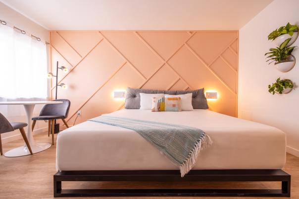 A vibrant, open guest room with minimalist retro styling, including a bedside reading nook, colorful geometric accents, and simple modern furnishings.