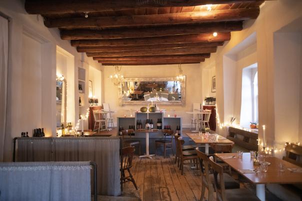 Cozy restaurant interior with wooden beams, soft candlelight, rustic decor, and tables set with glasses.