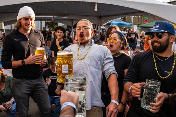 A crowd cheers as a man wearing a gold chain participates in a beer-drinking contest.