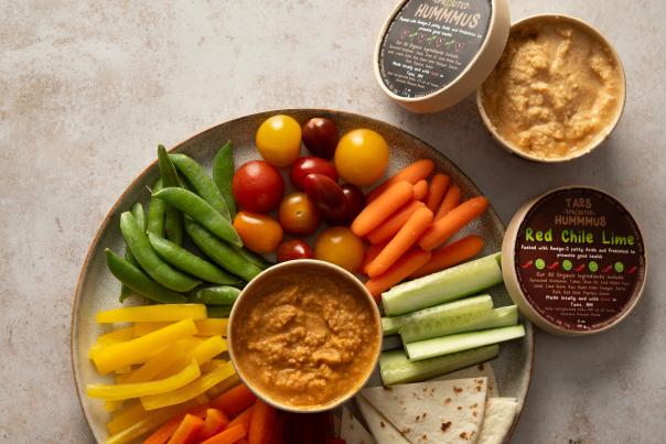 A round tray filled with colorful fresh veggies and two open containers of Taos Sprouted Hummus.