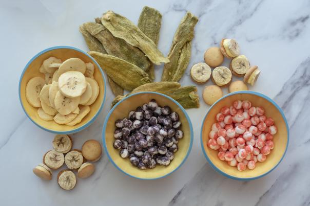 Colorful bowls of freeze-dried snacks including bananas, berries, and candies beside a bag of Hatch green chile Popped Candy.
