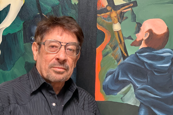Folklorist Ray John de Aragón, author and storyteller, stands in front of a colorful mural.