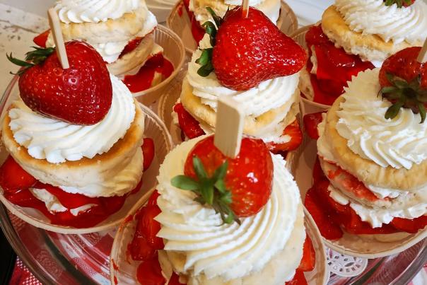 Several mini strawberry shortcakes topped with whipped cream and fresh strawberries are arranged on a glass platter.
