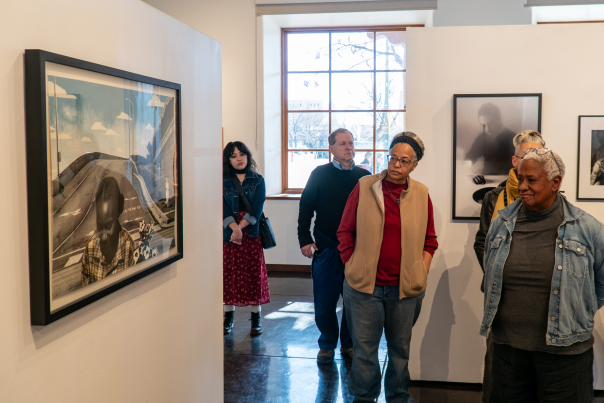 A diverse group of people attentively observe framed photographs in a well-lit art gallery.