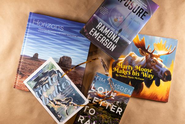 Five books with a pair of glasses lay scattered on a brown surface.