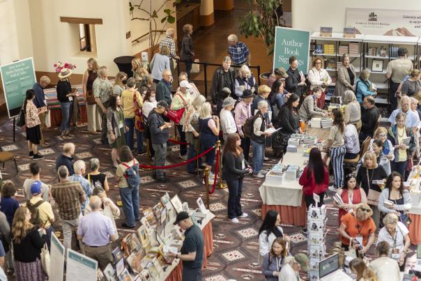 A large group of people attend a the Santa Fe International Literary Festival, gathered around tables with books.