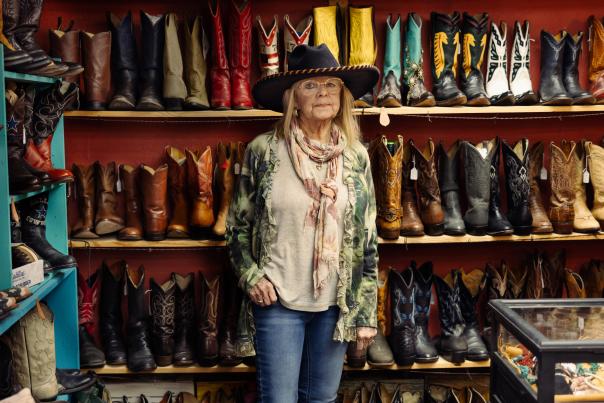 A woman in a cowboy hat stands in front of a wall of cowboy boots.