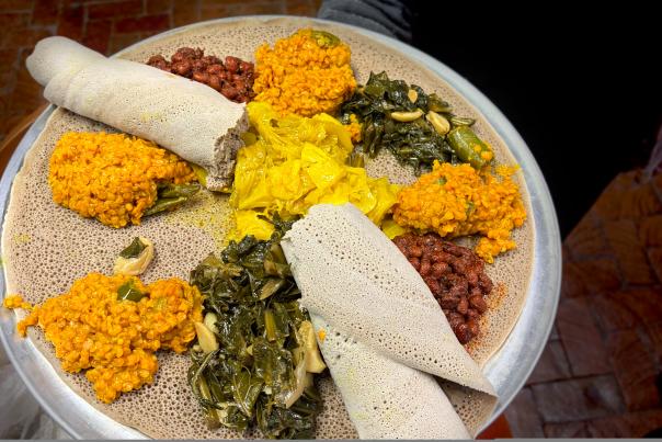 A platter of Ethiopian cuisine featuring various colorful dishes on injera, which is rolled at the edges.