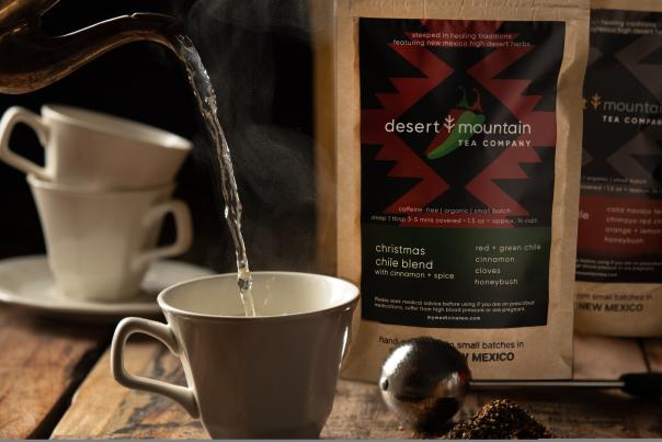 Hot water being poured into a teacup beside Desert Mountain Tea Company packaging.