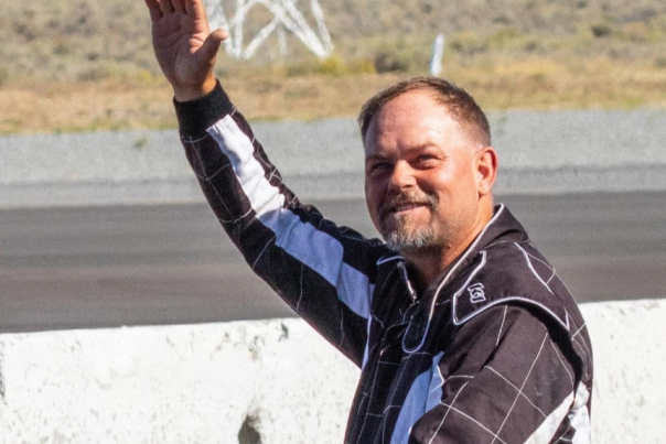 F1 air racing champion Josh Watson waves while wearing a black racing suit.