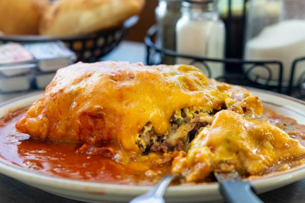 Cheesy enchiladas smothered in red sauce fill a plate with utensils on the side.