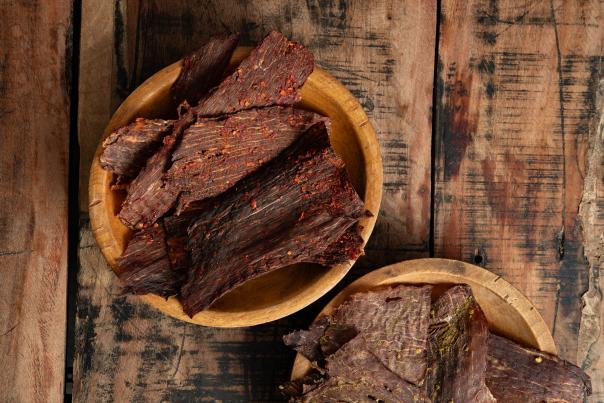 Two wooden bowls filled with seasoned beef jerky on a rustic wooden table.