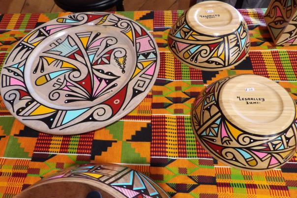 Colorful hand-painted wooden bowls and a plate with bold geometric designs displayed on a patterned textile.