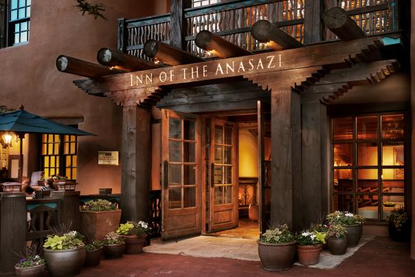Warm, welcoming hotel entrance with rustic wooden beams and soft lighting, surrounded by potted plants.