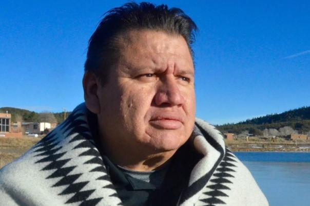 Man wrapped in a patterned blanket gazes contemplatively into the distance.