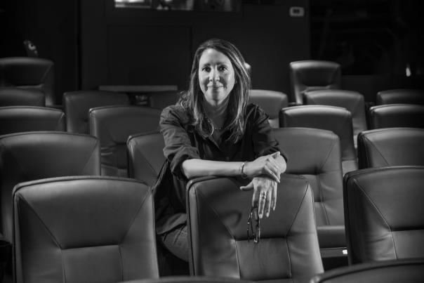 A person sits alone in a dimly lit theater, leaning forward over a row of empty seats.