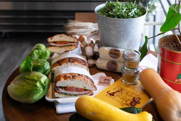 Artisan sandwiches, bread, and fresh produce arranged on a wooden table at Fable Market.