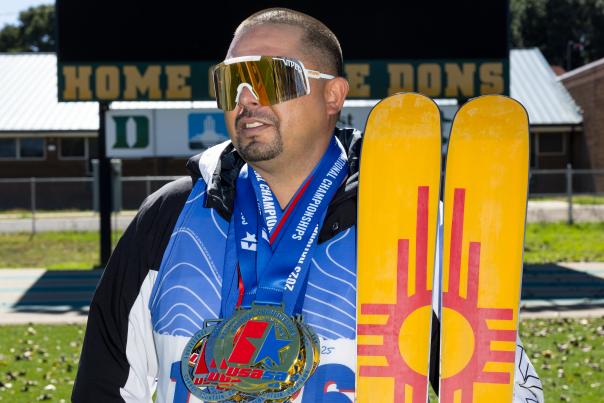 Edward Herrera holds skis with a Zia symbol while wearing racing medals.