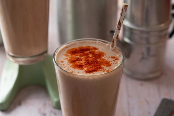 A tall glass filled with a creamy shake, topped with a sprinkle of red spice.