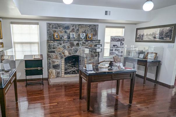 Interior of the Wingfield Heritage House Museum in Ruidoso featuring a large stone fireplaced, framed family photos, and display cases of historical artifacts.