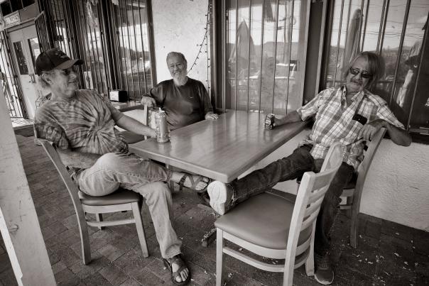 Three men gathered outside La Tiendita in Dixon, New Mexico, sharing drinks and conversation as part of the resolana tradition.