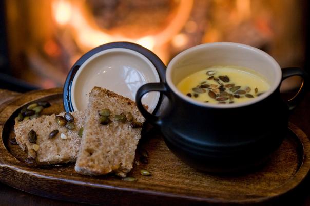 A bowl of soup served on a wooden tray with 2 slices of bread with an open fire out of focus in the background, at Grace Neill's Pub in Donaghadee, County Down.