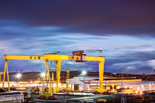 Harland and Wolff shipyard in Titanic Quarter at dusk. The 2 large  yellow Harland and Wolff cranes known as Samson and Goliath are prominent with the hangars illuminated in the background by lighting from the shipyard.