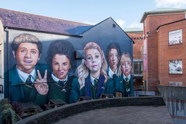 Mural of the main cast from TV's Derry Girls on the side of Badgers Bar in Derry/Londonderry. From left to right - James, Michelle, Erin, Orla, Claire. Michelle is giving a peace sign.