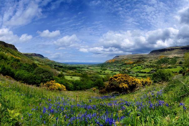 The image shows lush green hills and bright blue skies in the Glens of Antrim