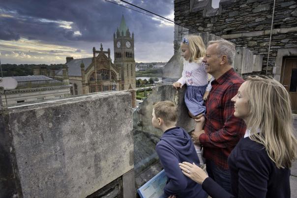 Family looks over the walls of Tower Museum, with Guildhall visible nearby
