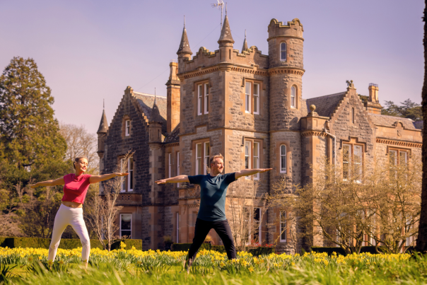A man and woman do a yoga pose in front of Elmfield Estate