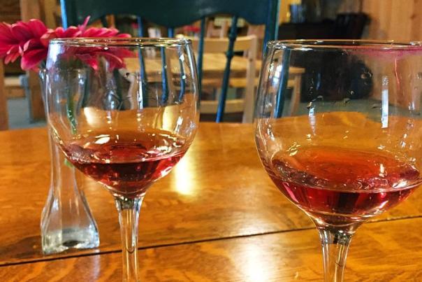 Two glasses of red wine on a wood table with red flowers