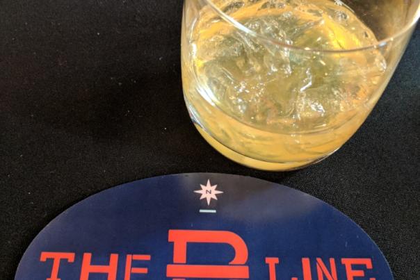 The B-Line cocktail in a bourbon glass next to a blue, red and white coaster for the B-Line