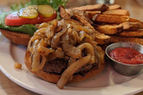 photo of a bison burger with caramelized onions and french fries served open faced on a plate