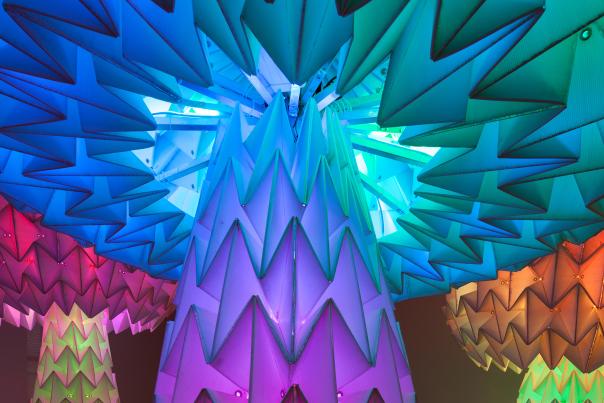 Elaborately folded paper mushrooms that are more than 12 feet high, illuminated with rainbow light, from Burning Man