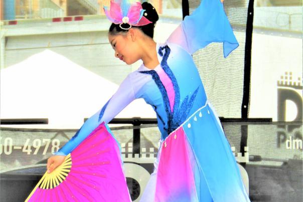 Young woman performing traditional Asian dance in a blue and pink outfit, using a large pink fan