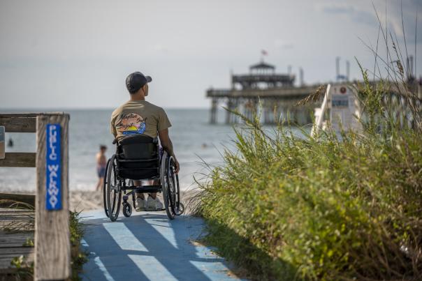 A man in a wheelchair looking at the Cherry Grove Pier from the beach
