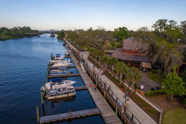 Scenic aerial view of the Barefoot Landing marina and boardwalk along the Intracoastal Waterway in North Myrtle Beach, South Carolina, with docked boats, palm trees, and waterfront dining.