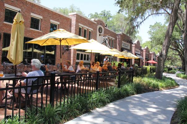 People sitting and drinking under umbrellas in outdoor dining area of Crooked Can Brewing Company at Plant Street Market in Winter Garden.